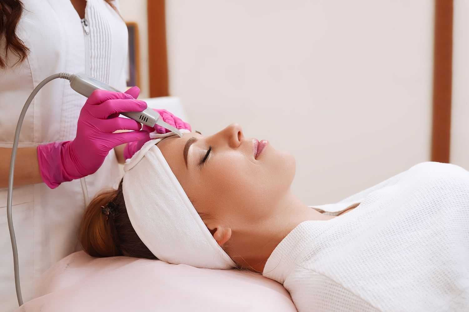 Facial treatment with a dermabrasion tool in a spa setting, woman relaxed on a bed.
