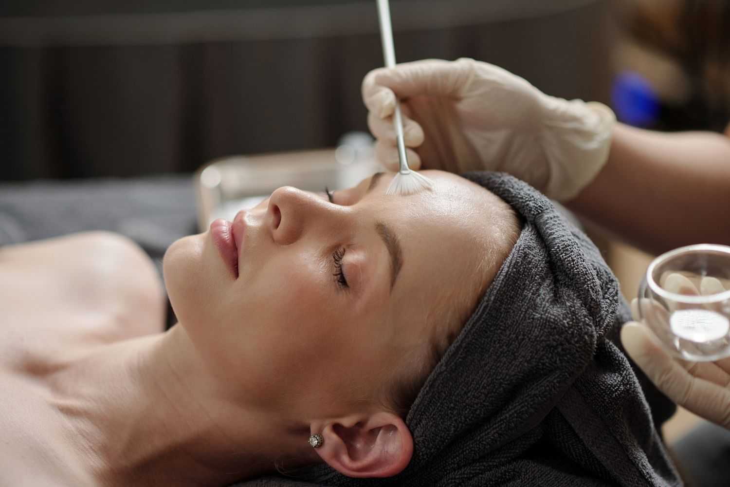 Person receiving a facial spa treatment with a brush, eyes closed, relaxed atmosphere.