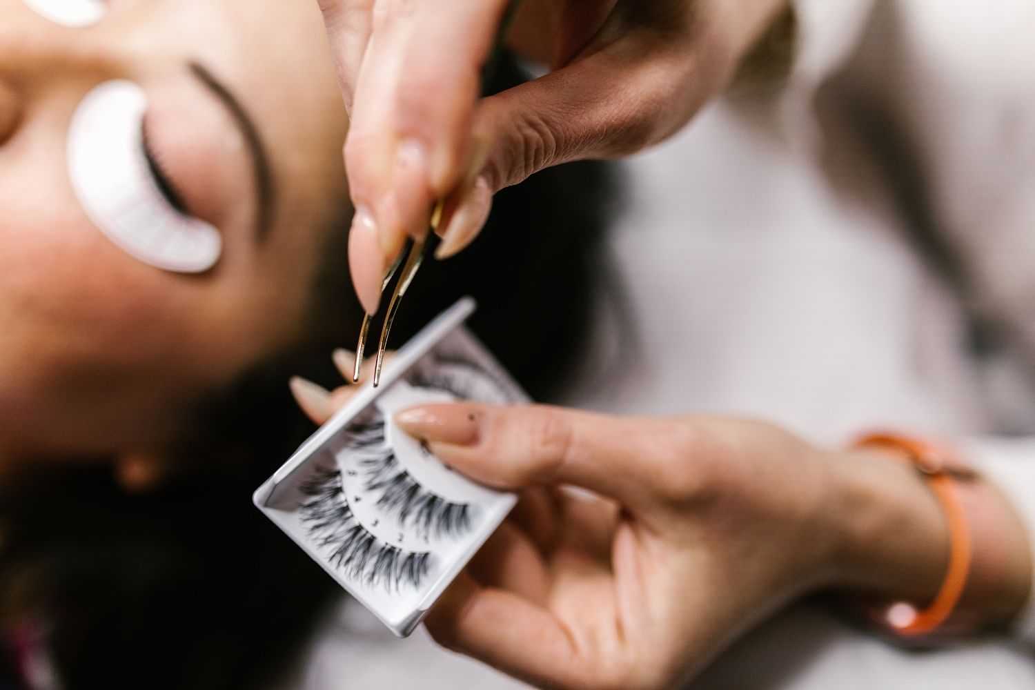 Applying eyelash extensions with tweezers to a person lying down in a beauty salon.