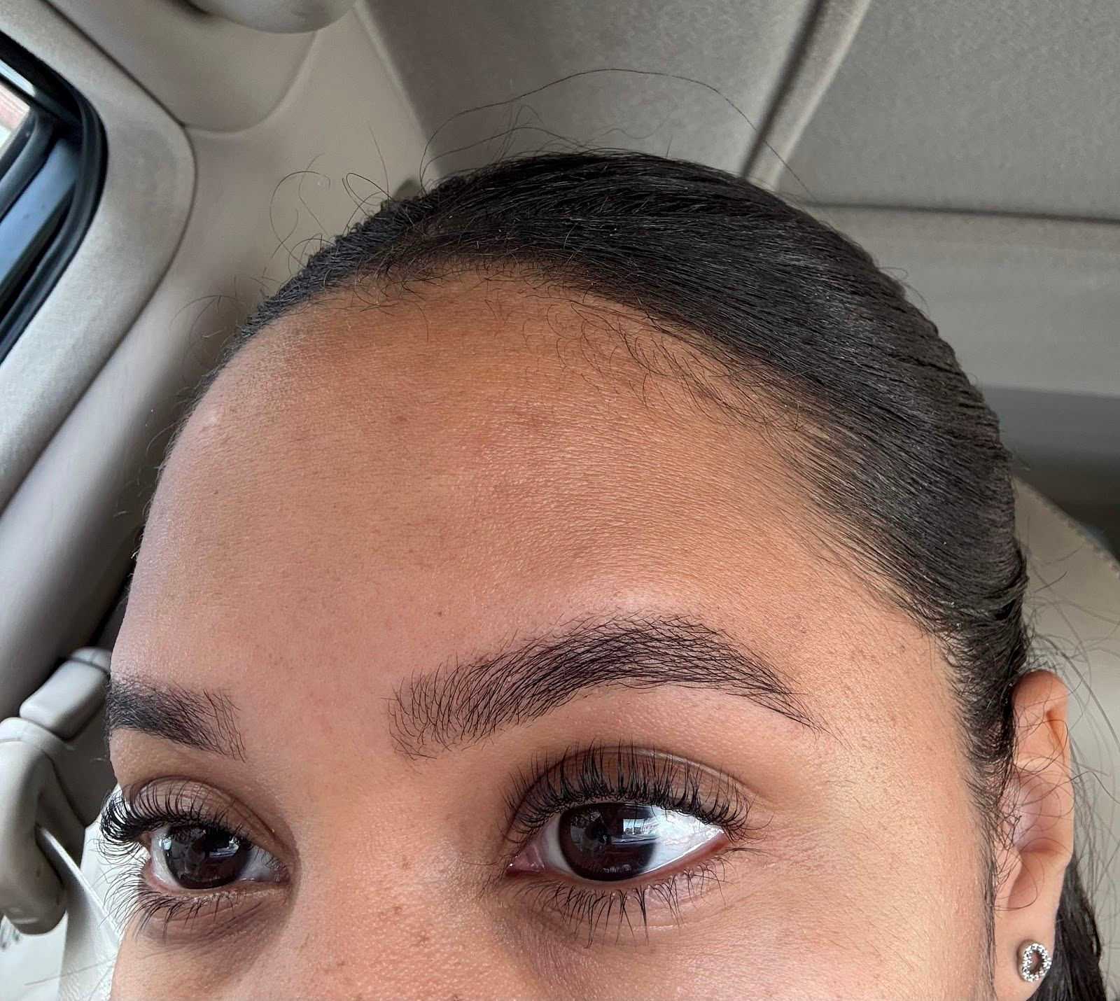 Close-up of a person's well-groomed eyebrows and eyelashes inside a car.