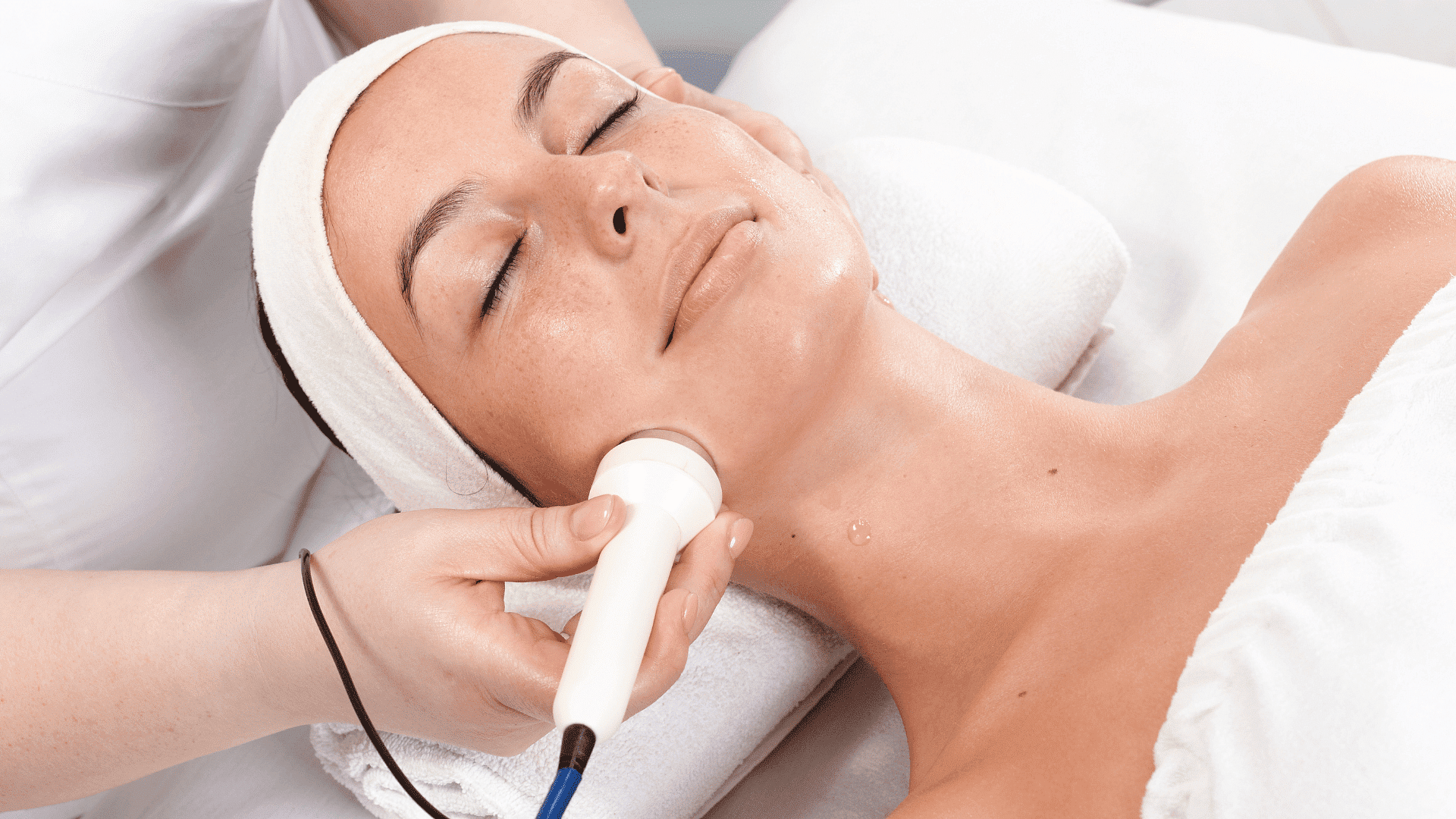 Facial treatment with a handheld device at a spa, relaxing in white towels.